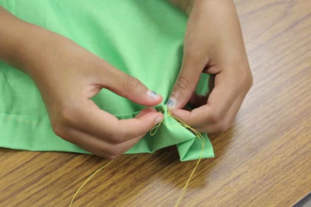 young child learning to sew