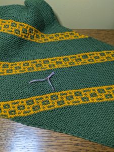 repaired hole in green and gold garter stitch shawl marked by waste yarn